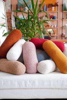 a pile of colorful pillows sitting on top of a white couch next to a potted plant