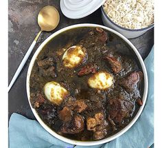 a bowl filled with meat and rice on top of a blue cloth next to two spoons