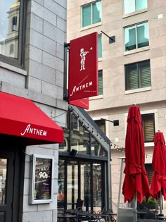 an outdoor restaurant with red umbrellas and tables in the foreground, on a city street