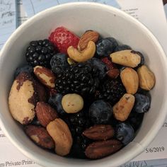 a bowl filled with nuts, berries and blueberries on top of a table next to papers