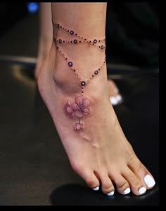 a close up of a person's foot with a flower on the ankle chain