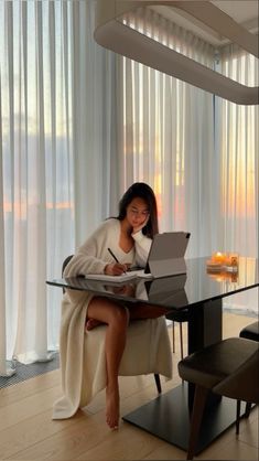 a woman sitting at a table with a laptop computer in front of her and writing