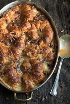 a casserole dish with meat and cheese in it on a wooden table next to two silver spoons