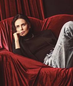 a woman laying on top of a red couch with her legs crossed and looking at the camera