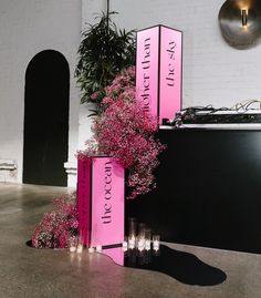 pink signs and candles are on display in front of a white brick wall with plants