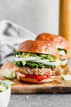 two chicken burgers with lettuce and tomato sauce on a wooden cutting board