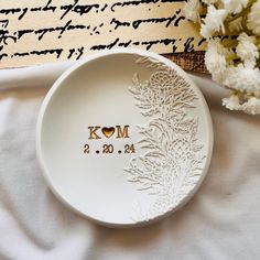 a white plate with the word kom on it next to some flowers and an old book