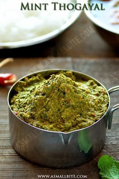 a metal pan filled with green food on top of a wooden table next to other plates