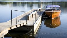 a boat docked at the end of a pier on a lake with trees in the background