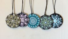 four different colored discs are hanging on a white wall with black cord and beadwork