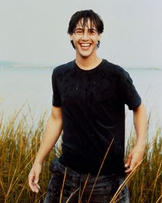 a young man standing in tall grass next to the ocean