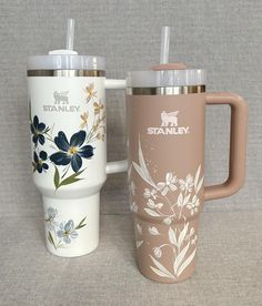 two travel mugs with matching lids and handles, one has flowers on the side