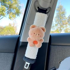 a stuffed animal hanging from the side of a car seat in front of a child's safety belt