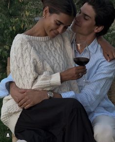 a man and woman sitting next to each other with a glass of wine in their hands