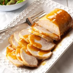 slices of sliced ham on a white plate next to a bowl of salad and fork