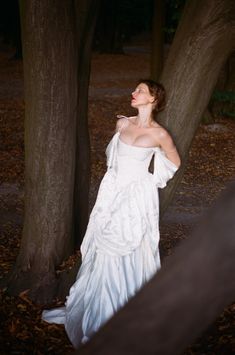 a woman in a white dress standing next to trees