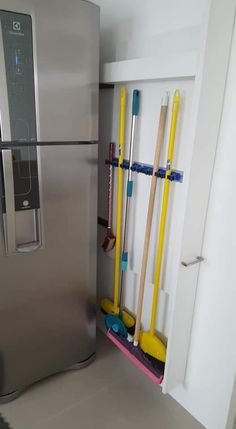 a metal refrigerator freezer sitting in a kitchen next to a rack with brooms and mop's