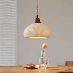 a wooden table topped with a glass vase filled with flowers next to a light fixture