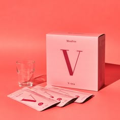 a pink box with four cards next to it and a glass filled with water on the table