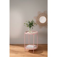 a small pink table with flowers on it and a mirror in the corner behind it