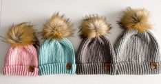 three knit hats with faux fur pom - poms are lined up against a white background