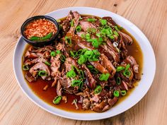 a white plate topped with meat covered in sauce and garnished with green onions