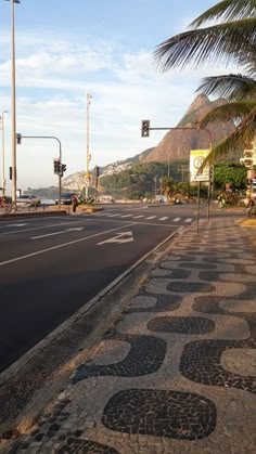 an empty street with palm trees on both sides and mountains in the distance behind it