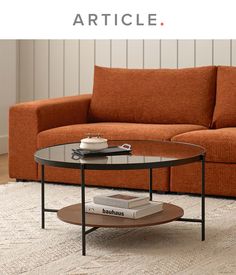 a living room with an orange couch and coffee table on the floor, in front of a white wall