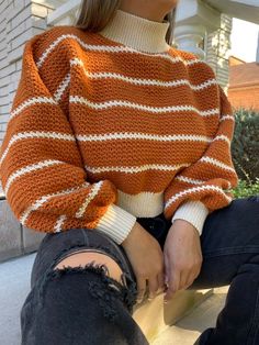 a woman wearing an orange and white striped sweater sitting on the ground with her legs crossed