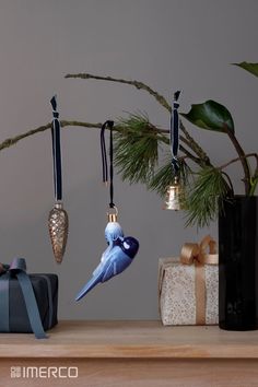 a blue bird ornament hanging from a branch next to presents and a christmas tree