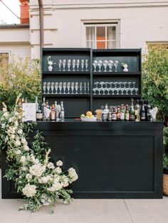 an outdoor bar with bottles and glasses on the top shelf, surrounded by greenery