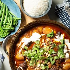 a bowl filled with stew next to rice and broccoli on a wooden table