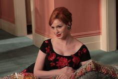 a woman with red hair is sitting on a couch and looking off to the side