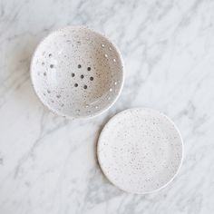 two white speckled bowls sitting on top of a marble counter