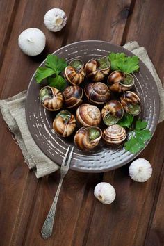 a plate filled with lots of clams on top of a wooden table next to garlic and parsley