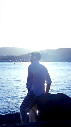 a man sitting on a rock looking out over the water with his back to the camera