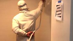 a man in a white outfit is using a power washer on the bathroom wall