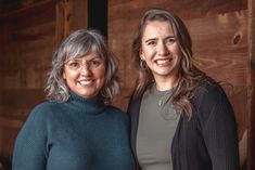 two women standing next to each other in front of a wooden wall with wood paneling