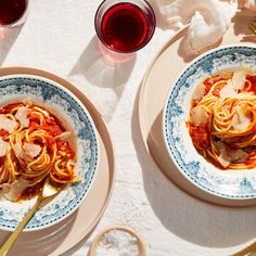 two plates of pasta with sauce and parmesan cheese next to glasses of wine