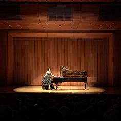 a woman sitting at a piano in front of a stage with an audience looking on