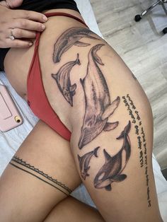 a woman laying on top of a bed next to two dolphins tattoo design on her thigh