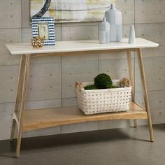 a white table with a basket and vases on it in front of a wall