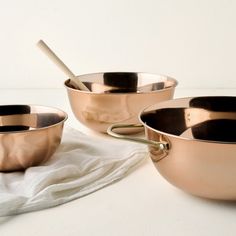 three copper colored bowls with spoons in them on a white tablecloth next to each other