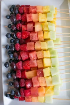 fruit skewers are arranged on a white platter, ready to be eaten