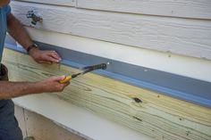 a man holding a pair of pliers in front of a house with siding on it