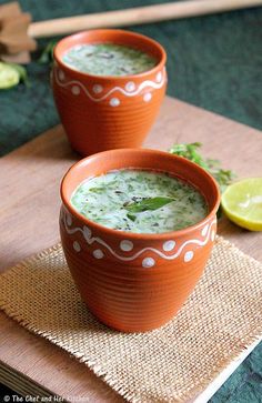 two orange bowls filled with broccoli soup on top of a wooden cutting board