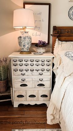 a white dresser sitting next to a bed on top of a hard wood floor under a lamp