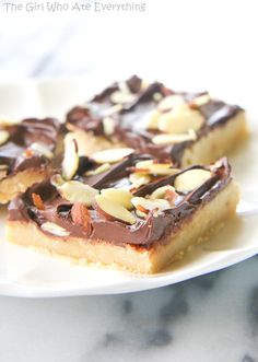 two pieces of chocolate and almond bars on a white plate next to a marble counter