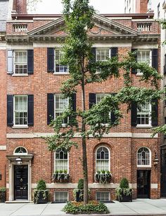 an old brick building with black shutters on the windows and trees in front of it