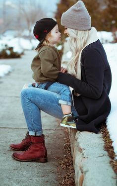 a mother and her child are sitting on a bench in the snow with their noses to each other